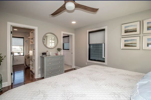 Modern bedroom with neutral tones, a ceiling fan, and a dresser with a round mirror.