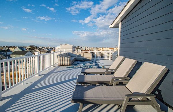 Spacious rooftop deck with lounge chairs and a sectional sofa under a blue sky.