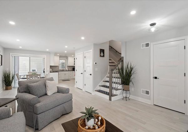 Bright and modern living room with gray furniture and a view into the kitchen and dining area.