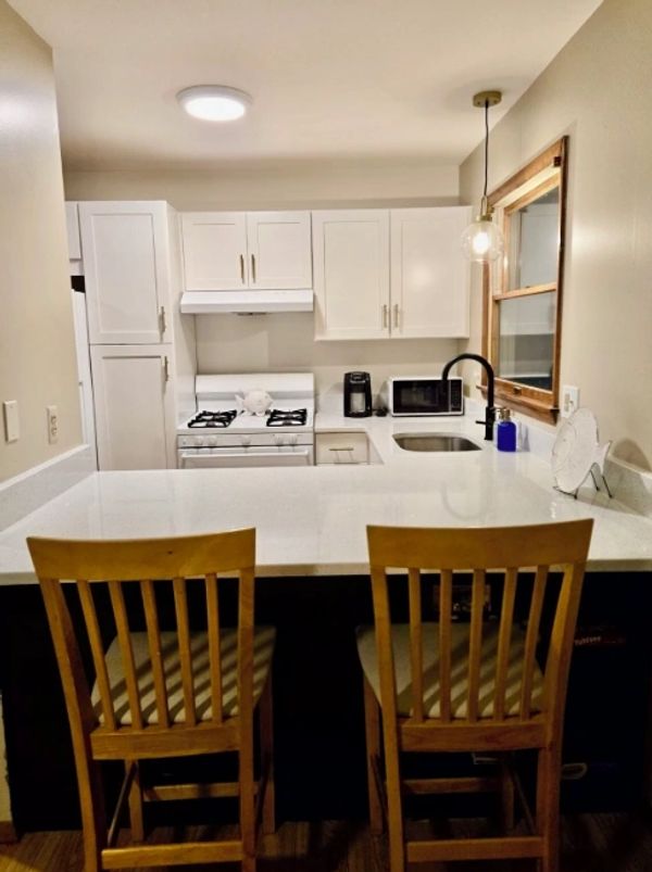 Cozy kitchen with white cabinets, wooden chairs, and modern appliances.