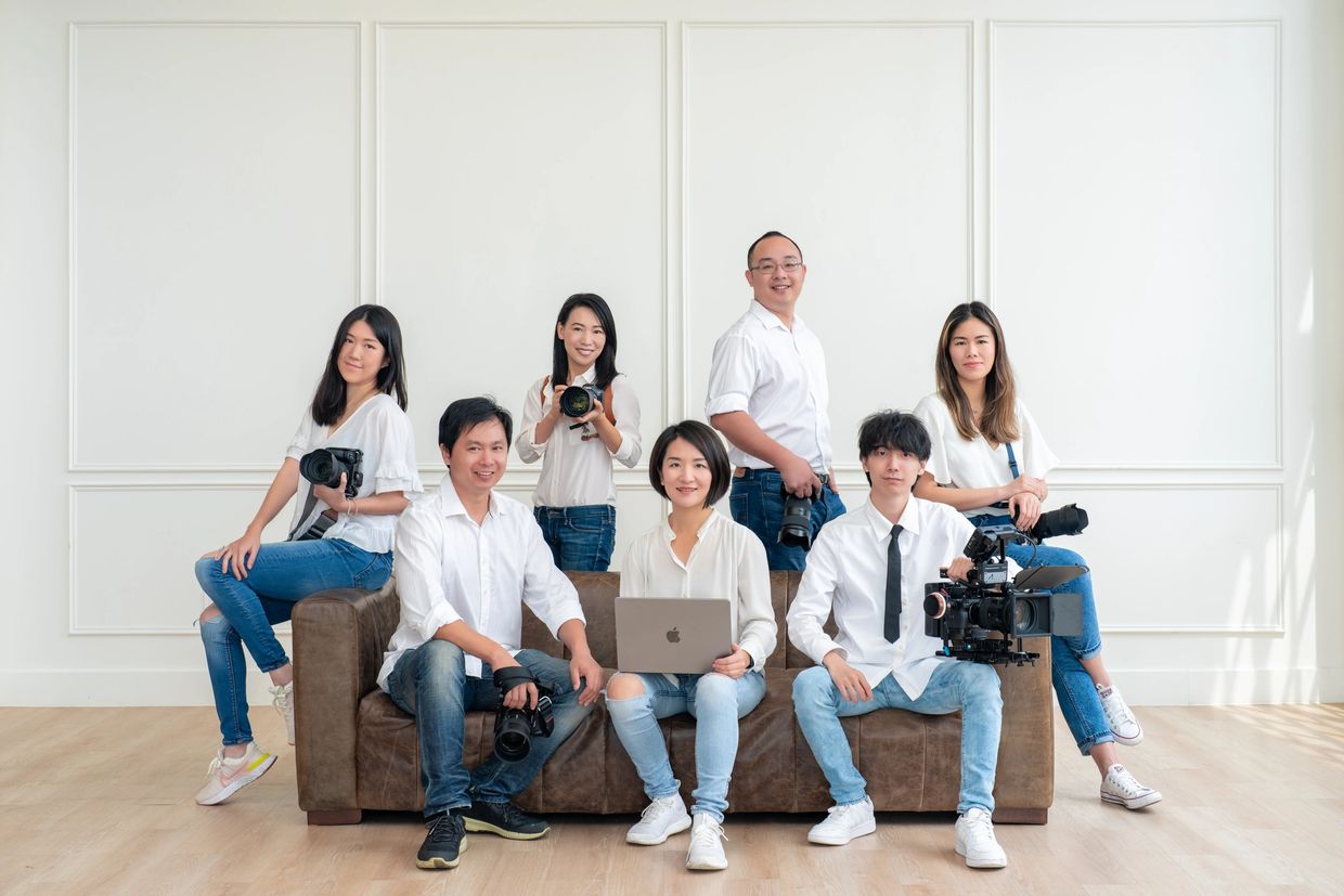 Group of photographers and videographers posing with cameras and laptop indoors.