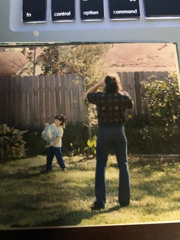 Child and adult in a backyard with a wooden fence and greenery.