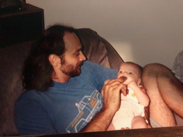 A man lovingly feeding a baby while sitting on a couch.