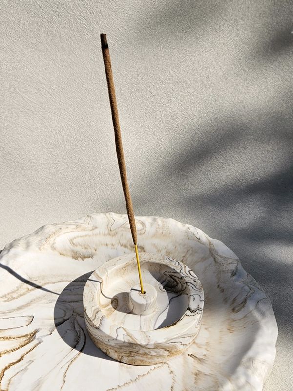Marble incense holder with a lit incense stick casting shadows.