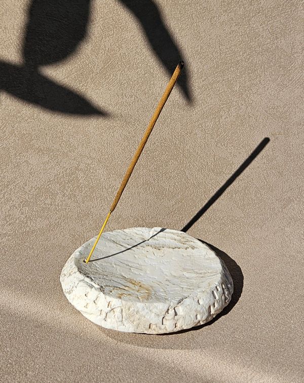 A burning incense stick in a white holder casting a shadow.