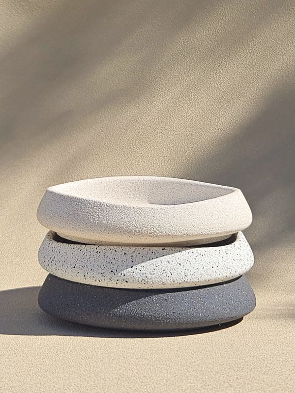 Three stacked minimalist stone bowls in neutral tones with textured surfaces.