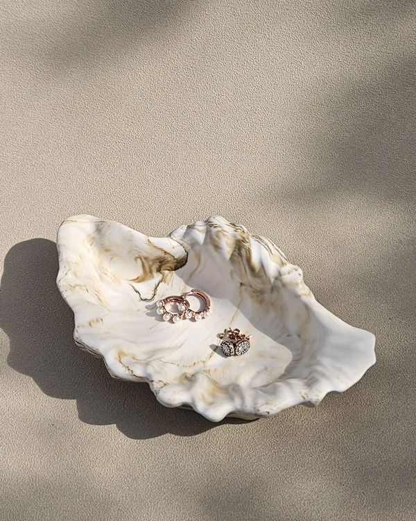 Decorative shell dish holding elegant rings on a textured surface.