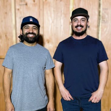 Two men smiling, wearing caps and casual t-shirts.