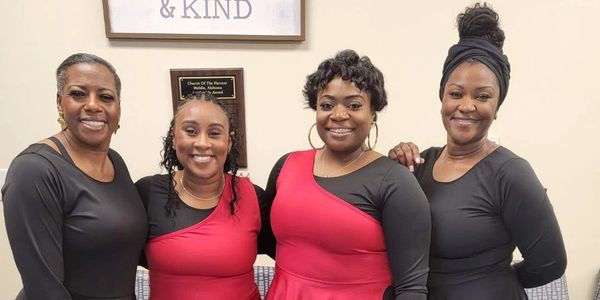 Four women smiling, two in red and black outfits, two in black.