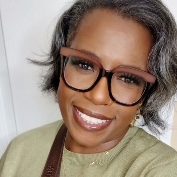 Smiling woman wearing large glasses and a green sweater.