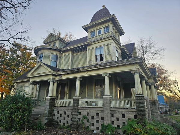 Old, abandoned Victorian-style house with peeling paint and broken windows.