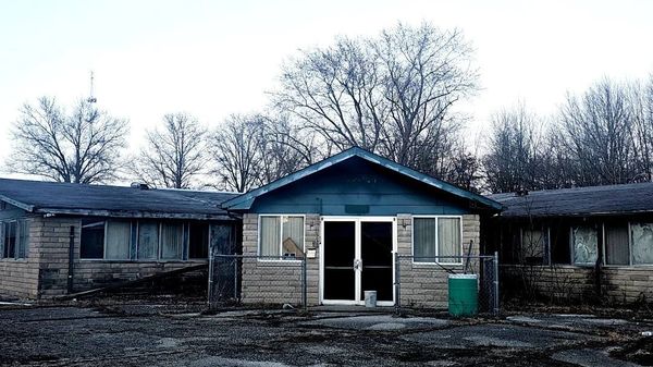 Abandoned building with boarded windows and overgrown surroundings.