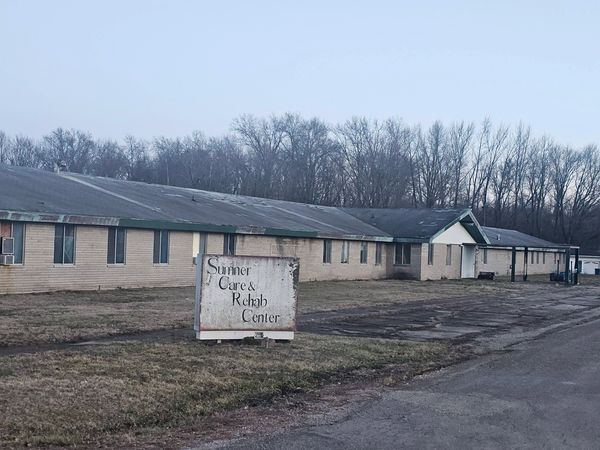 Exterior of Sumner Care &amp; Rehab Center with worn sign and long building.