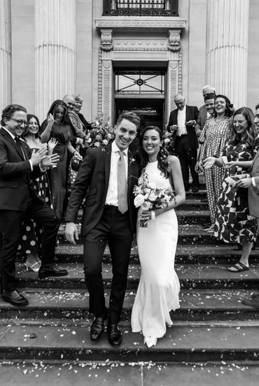 Newlyweds joyfully walk down church steps surrounded by cheering guests.