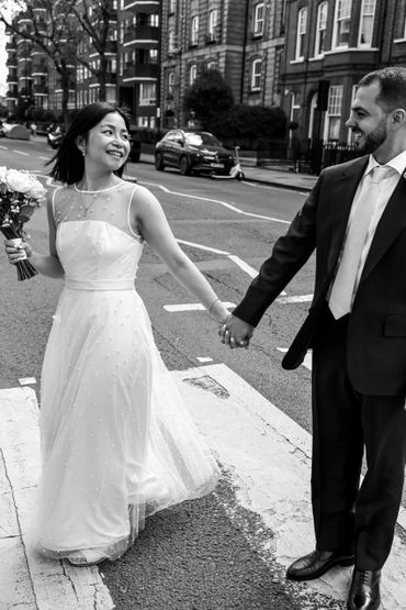 Bride and groom smiling at each other while holding hands on a city street.