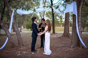 Couple exchanging vows in an outdoor wedding ceremony under a floral arch.