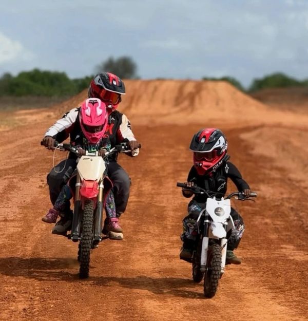 Two riders on dirt bikes riding on a dirt track with helmets on.