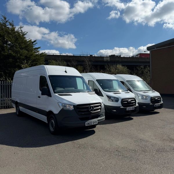 Three white delivery vans parked side by side under a blue sky.