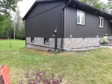 Modern house with black siding and stone foundation.
