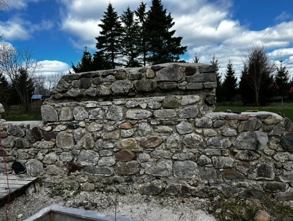 Old stone wall outdoors with trees and sky.