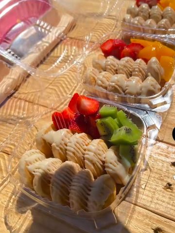 Heart-shaped containers with waffles, strawberries, kiwi, and mango, drizzled with cream.
