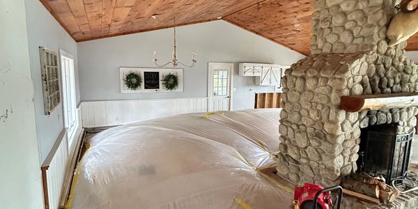 Plastic containment tent set up in a rustic room with a stone fireplace and wooden ceiling.