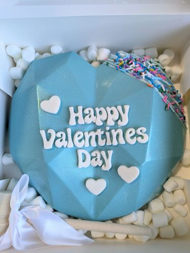 Blue heart-shaped cake with "Happy Valentines Day" text and colorful sprinkles.