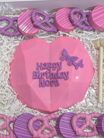Pink heart-shaped cake with purple lettering and butterfly decoration for Nora's birthday.
