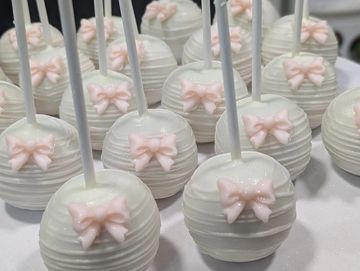 White cake pops with delicate pink bows on sticks.