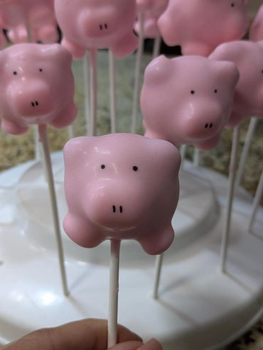 Pink pig-shaped cake pops on sticks, arranged on a white stand.