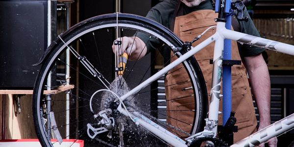 Man cleaning a white bicycle's rear wheel in a workshop.