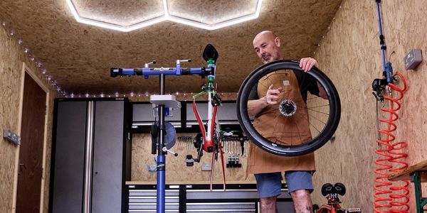 Man holding a bicycle wheel in a workshop.
