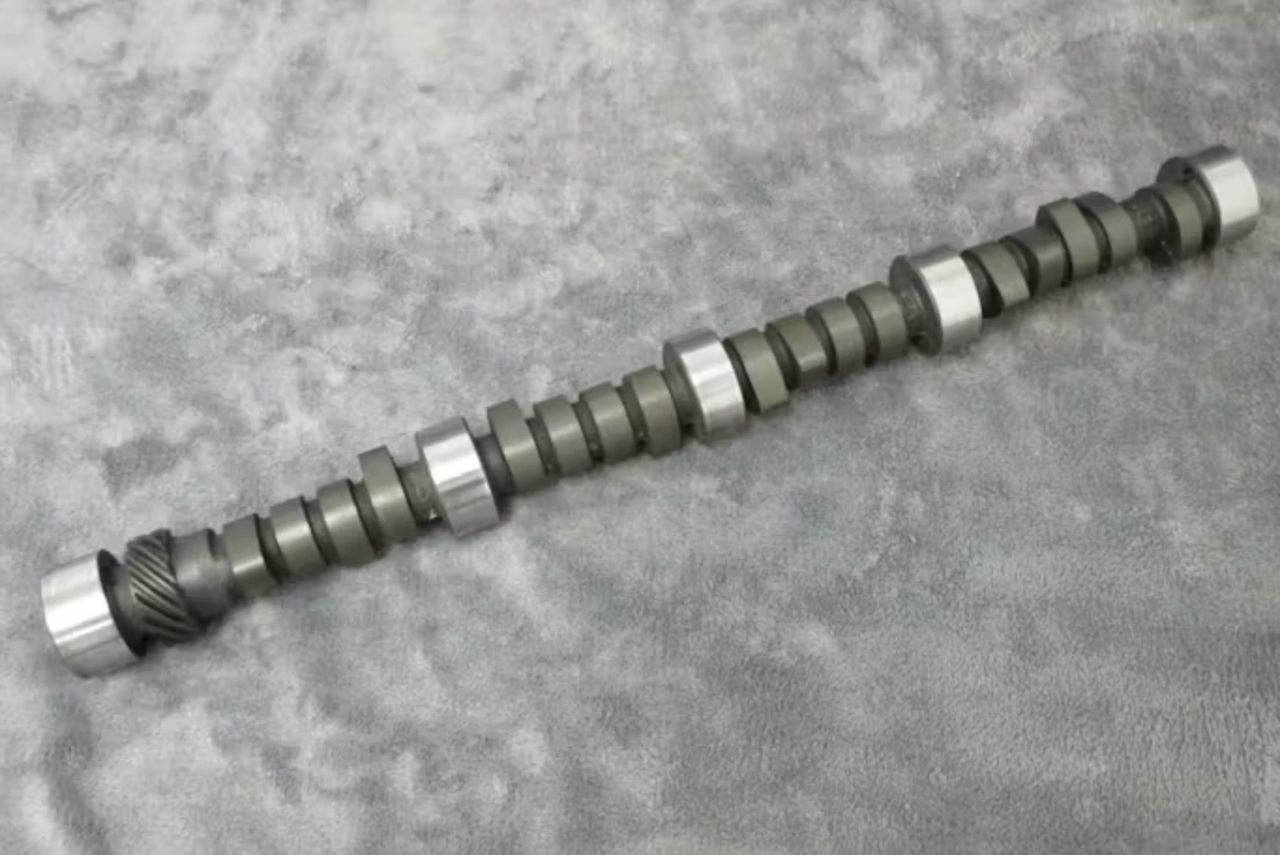The “Duntov cam,” officially GM part number 3736097 and commonly known as the 097, became one of the most influential performance camshafts of the early small-block era. Introduced for Chevrolet’s solid-lifter V8s in the late 1950s, it featured approximately .447 inches of valve lift with 1.5:1 rockers, duration in the high-220° range at .050-inch lift, and a relatively wide lobe separation intended to balance high-rpm power with durability. Zora Arkus-Duntov developed the profile to improve airflow and extend usable engine speed, directly addressing the breathing limitations he encountered during early Corvette performance testing, including work tied to the EX-87 program. Unlike peaky racing grinds of the era, the 097 cam delivered a broad, usable powerband that could survive sustained high-rpm operation. Its success cemented Duntov’s philosophy that reliable horsepower came from controlled valvetrain dynamics, not excess. Decades later, the cam remains a benchmark—proof that thoughtful engineering can define an entire generation of performance. (Image source: Chevy Hardcore.com)