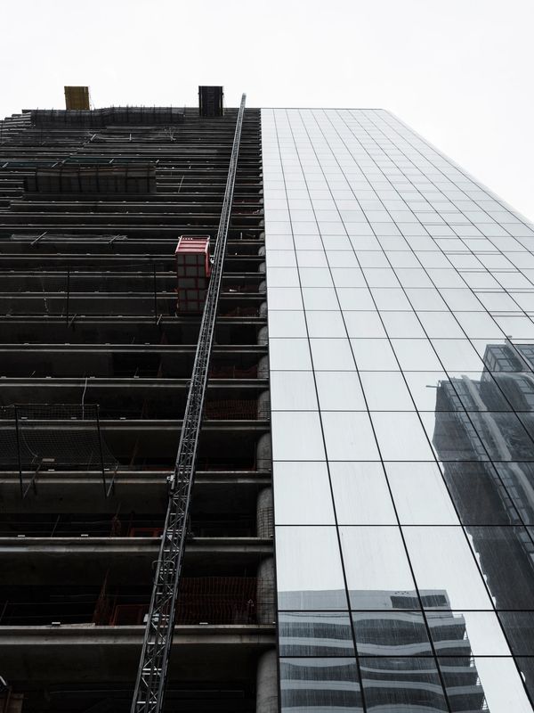 A building under construction with a glass facade reflecting nearby structures.