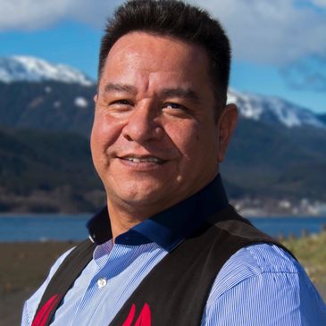 Man smiling outdoors with mountains in the background.