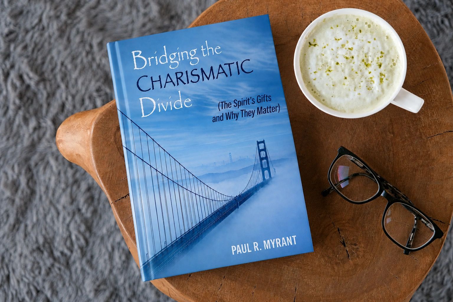 Book titled 'Bridging the Charismatic Divide' on a wooden table with coffee and glasses.