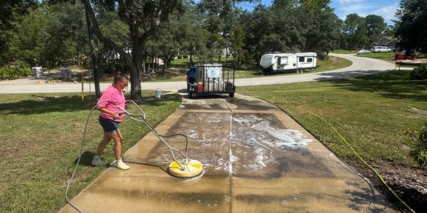 Person pressure washing a driveway on a sunny day.