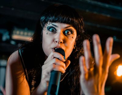 A singer with dramatic eye makeup passionately performs with a microphone.