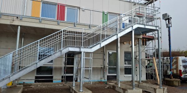 Metalltreppe an einem Gebäude unter bewölktem Himmel.