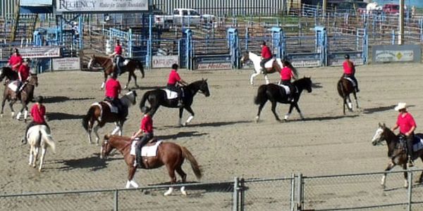 Group of people on horseback in a rodeo arena.