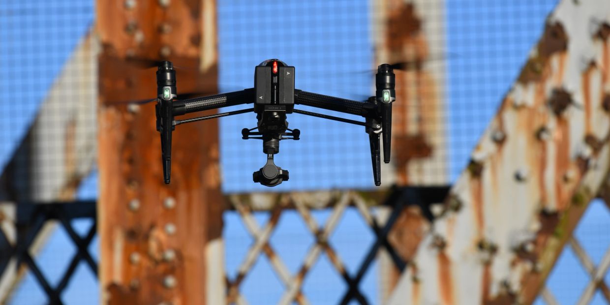Drone flying near a rusty metal structure.