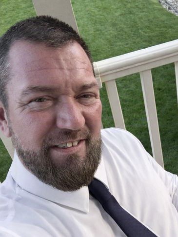 Smiling man in white shirt and black tie outdoors.