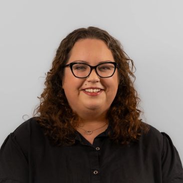 Smiling woman with curly hair and glasses.