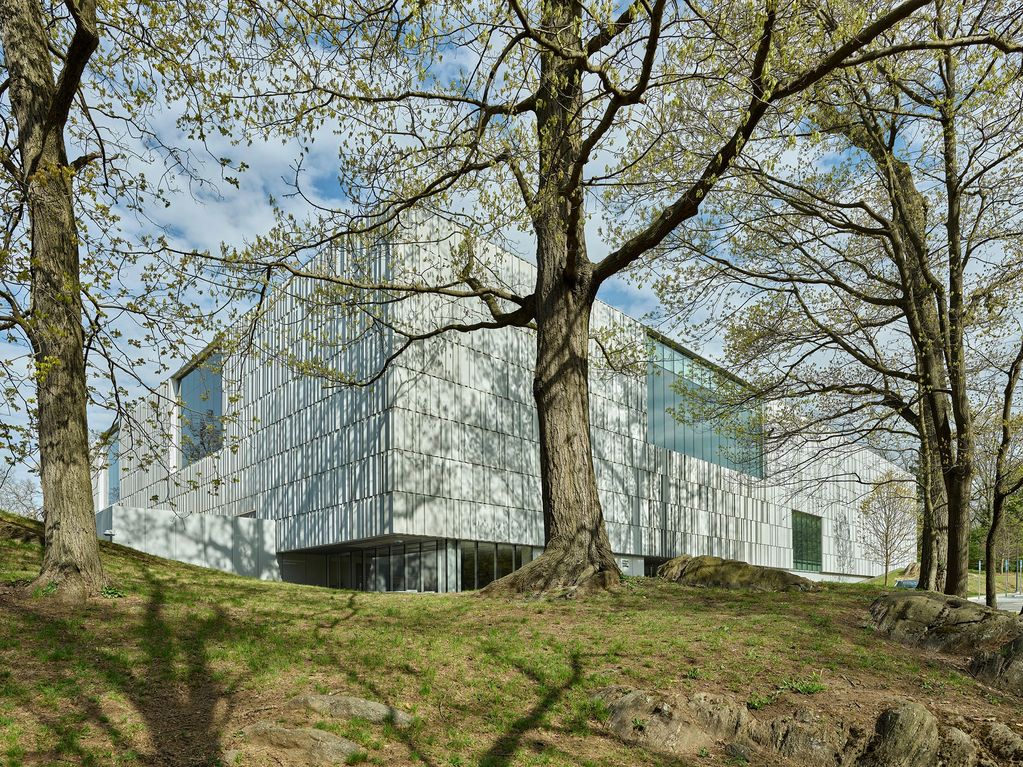 Modern building behind trees on a grassy hill.