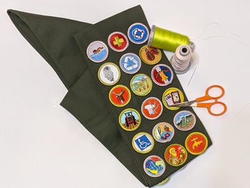 A green scout neckerchief with colorful merit badges and sewing supplies.