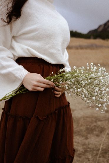Person holding delicate white flowers in a rustic outdoor setting.