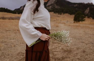 Woman holding a bouquet of small white flowers in a dry field.