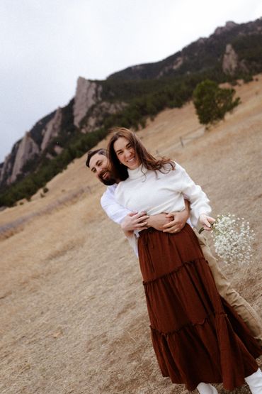 Couple embracing outdoors with mountains in the background.
