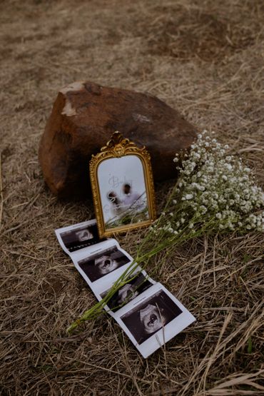 Ultrasound photos, a flower bouquet, and a framed message on dry grass.
