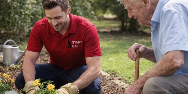 Young caregiver helps elderly man plant flowers in garden.